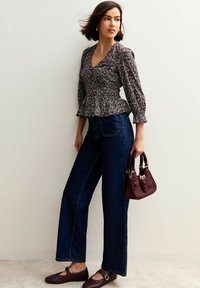 Bloemrijke peplumblouse met driekwartmouwen, gecombineerd met high-waisted donkerblauwe wijde jeans. Bordeauxtassen en bruine flats.