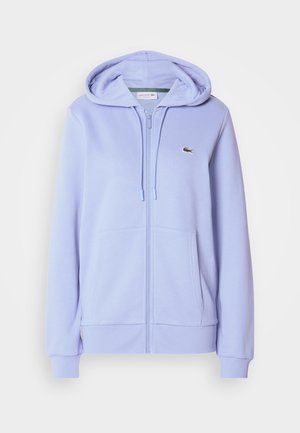 Lila Kapuzenjacke mit Reißverschluss aus weichem Stoff, mit Kängurutasche und Kapuze mit Kordelzug. Kleines, aufgesticktes Logo auf der Brust.