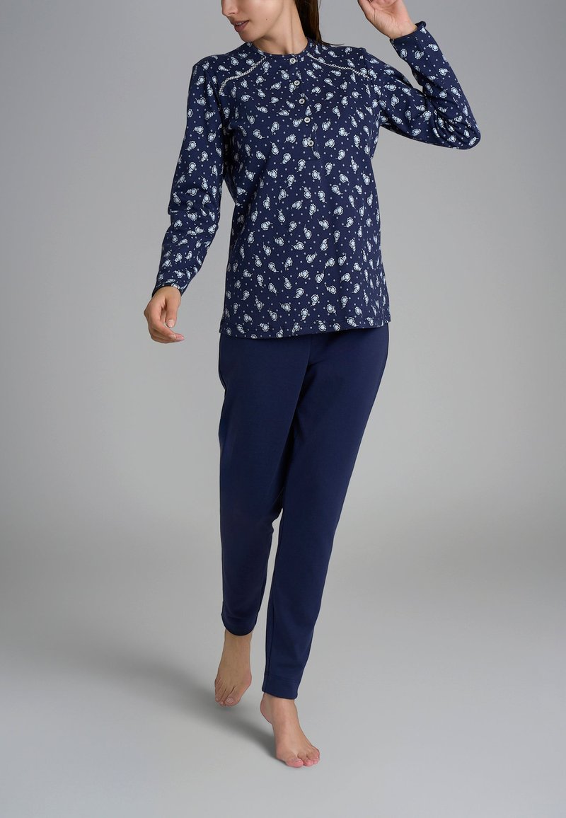 Maglia a maniche lunghe blu navy decorata con piccoli motivi floreali bianchi, abbinata a pantaloni blu navy. Il tessuto sembra morbido e leggero. Modella che cammina a piedi nudi.