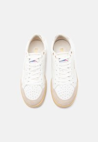 Λευκά αθλητικά παπούτσια με δερμάτινο επάνω μέρος με υφή, διάτρητη μύτη, μπεζ σουέντ λεπτομέρειες και λευκά κορδόνια. Χρυσά μεταλλικά τρύπια και διακριτικές λεπτομέρειες με το λογότυπο.