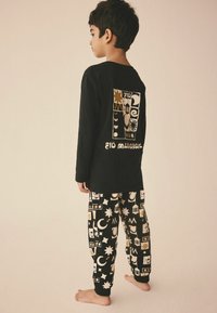 Schwarzes Langarmhemd mit goldenem, am Rücken aufgedrucktem Eid-Themen-Motiv, kombiniert mit passenden schwarzen Hosen, die verschiedene goldene Symbole und Muster aufweisen.