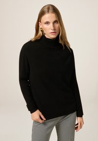 Maglione nero a collo alto realizzato in tessuto morbido, con maniche lunghe. Abbinato a pantaloni a scacchi grigi e bianchi con motivo.