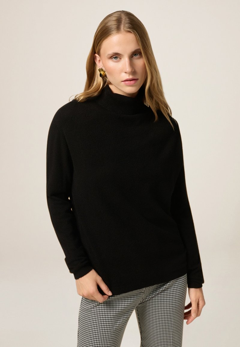 Maglione nero a collo alto realizzato in tessuto morbido, con maniche lunghe. Abbinato a pantaloni a scacchi grigi e bianchi con motivo.
