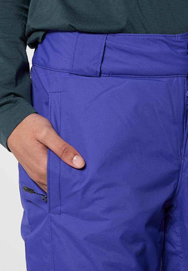 Pantaloni isolati viola con tasche laterali, realizzati in tessuto testurizzato. Presentano una cintura liscia e un dettaglio con zip su una tasca.