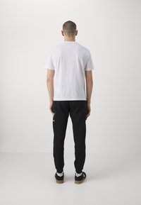 White cotton t-shirt with short sleeves, paired with black sweatpants featuring a graphic pattern and elastic cuffs, worn with black sneakers.