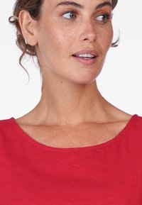 Red short-sleeve top with a wide scoop neckline, made from a textured fabric. Features subtle detailing on the edges and a relaxed fit.