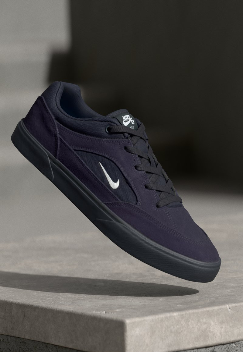 Nike SB gördeszkás cipők sötétlila velúr és hálós anyagból, fehér pipa logóval, fekete fűzőkkel és alacsony profilú kialakítással, textúrázott talppal.