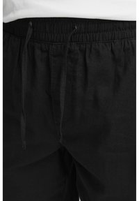 Pantalons noirs à cordon de serrage en tissu doux, dotés d'une taille élastique et de détails de couture visibles.