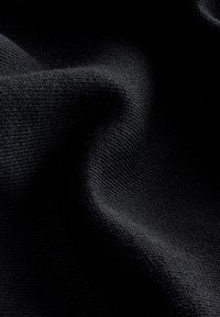 Gros plan sur un tissu tricoté noir avec des plis doux et une texture visible mettant en valeur le motif de tissage et les fibres.