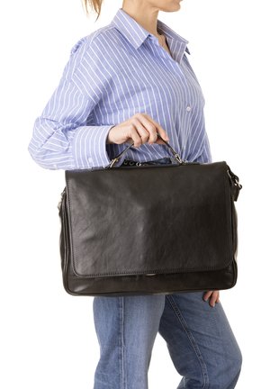 Vrouw in een blauw gestreept shirt en spijkerbroek die een grote zwarte leren aktetas bij het handvat vasthoudt.