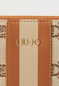 Tan and beige striped handbag with a woven texture. Features a logo tag and gold hardware. Zipper closure at the top.