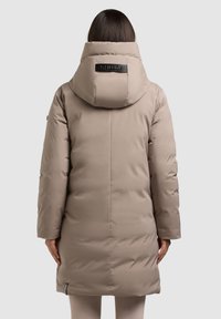 Beidzīgas krāsas pūkainais mētelis ar augstu apkakli un logo detaļu aizmugurē. Izturīgs, ar garām piedurknēm un gludu, nedaudz teksturētu virsmu.