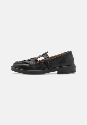 Schwarze Leder-Schuhe mit einem geflochtenen Muster, T-Riegel-Design und einer seitlichen Schnalle. Sie haben einen niedrigen, abgerundeten Absatz und eine glatte Textur.