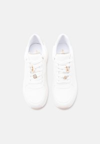 Baskets blanches avec une tige texturée, des accents en métal doré et des lacets. Comprend des breloques florales et géométriques attachées aux lacets.