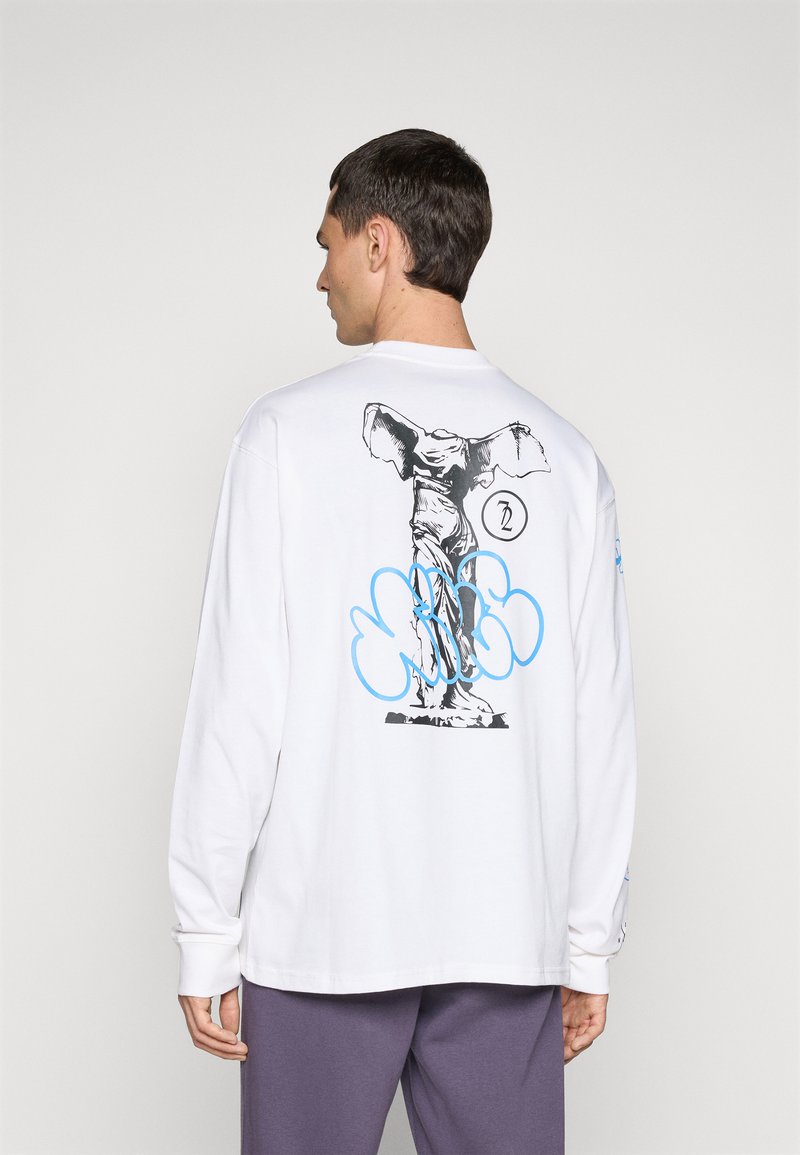 T-shirt blanc à manches longues avec un graphique noir et bleu d'une statue au dos, accompagné d'accents en bleu en forme de nuages et d'un logo circulaire.