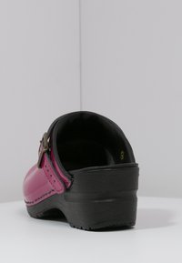 Pink clogs with a glossy finish, black rubber sole, and textured heel. Features a side buckle and a rounded toe design.