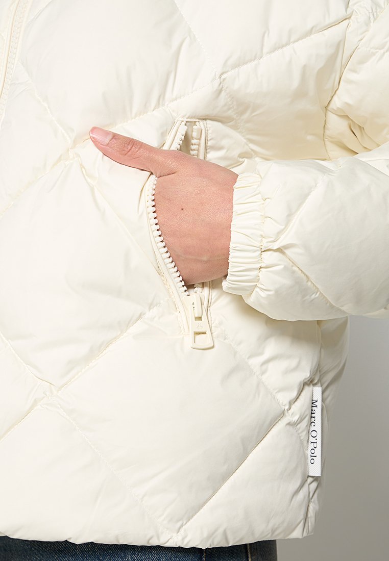 Witte pufferjack met een geborduurd ontwerp, ritszak, elastische manchetten en een merklabel aan de zijkant. Soepele, gevoerde textuur.