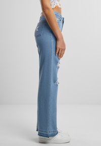 Svetlo modr�é džíny s rovnými nohavicami a so zničenými detailmi, majú vysoký pás a strapcový lem, skombinované s bielymi teniskami.