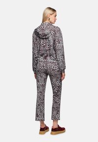 Trainingsanzug mit Leopardenmuster und Kapuze; weicher Stoff, eng anliegende Passform, mit elastischem Bund. Kombiniert mit roten Plateauschuhen.