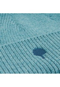 Gestructureerde blauwe stof met een geribbeld patroon, voorzien van een kleine silhouet van een donkerblauwe boom. Het materiaal lijkt zacht en licht pluizig.