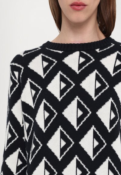 Pulover tricotat cu un model geometric de diamante alb-negru, cu accente triunghiulare, decolteu rotund și manșete cu nervuri.