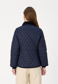 Quilted navy jacket with a collar, featuring diamond pattern and contrasting dark trim. Displayed from the back, showing side pockets.