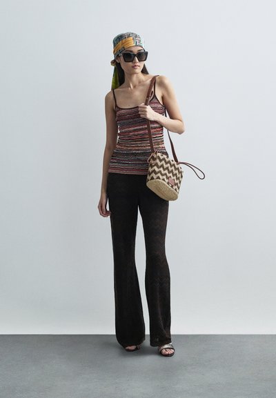Ριγέ πλεκτή αμάνικη μπλούζα, μαύρο παντελόνι με σχέδιο τσέβρον και φαρδύ τελείωμα, πλεκτή στρογγυλή τσάντα και μεγάλα γυαλιά ηλίου, συμπληρωμένα με ένα πολύχρωμο μαντήλι.