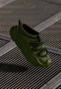 Zielone sportowe buty z zaokrąglonym czubkiem, teksturowaną powierzchnią, elastycznymi sznurowadłami i gumową podeszwą. Lekka konstrukcja z wzmocnionymi detalami.