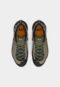 Ζευγάρι πεζοπορικά παπούτσια σε ελιά πράσινο και μαύρο με κορδόνια, πορτοκαλί εσωτερικά πέλματα με την ένδειξη "CFF" και θηλιές τράβηγματος με την επιγραφή "UNITES ENG".