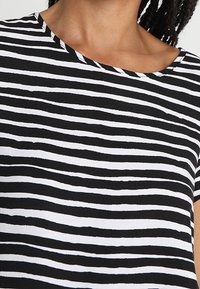 Mujer vestida con una blusa de rayas horizontales en blanco y negro con escote redondo, mostrando solo el cuello y la parte superior del pecho.