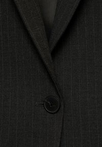 Veste de costume gris foncé à fines rayures avec un revers cranté et un seul bouton noir fermé au centre devant.