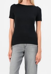 Černé tričko s krátkým rukávem a lodičkovým výstřihem, vyrobené z hladké tkaniny. Slučuje se se světlými šedými širokými džíny. Jednoduchý a přiléhavý design.