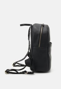 Black leather backpack with textured surface, gold zipper, and adjustable straps featuring a logo print. Slim shape with side pocket.