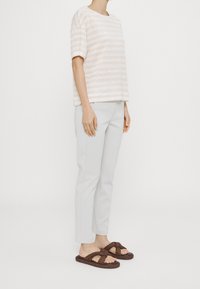 Blusa corta de mangas cortas con rayas claras, color beige pálido, combinada con pantalones grises claros de corte a medida y sandalias de slide tejidas marrones con detalle de nudo.