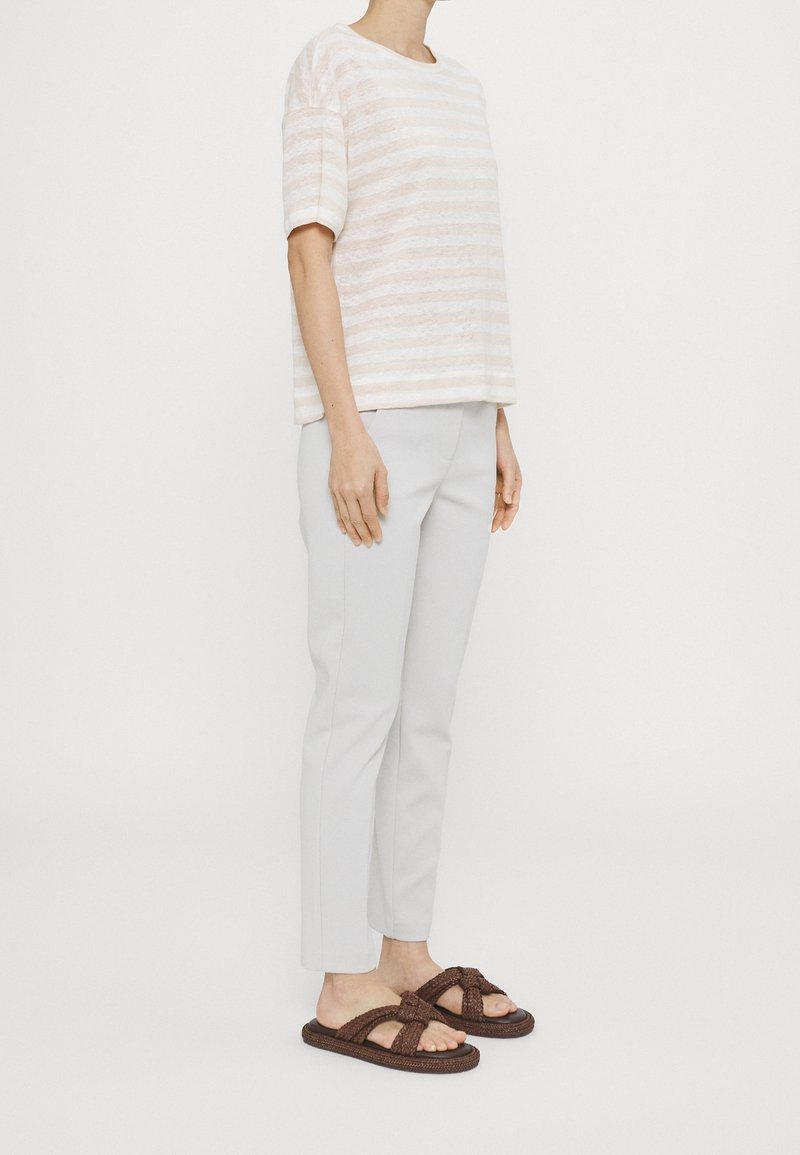 Blusa corta de mangas cortas con rayas claras, color beige pálido, combinada con pantalones grises claros de corte a medida y sandalias de slide tejidas marrones con detalle de nudo.