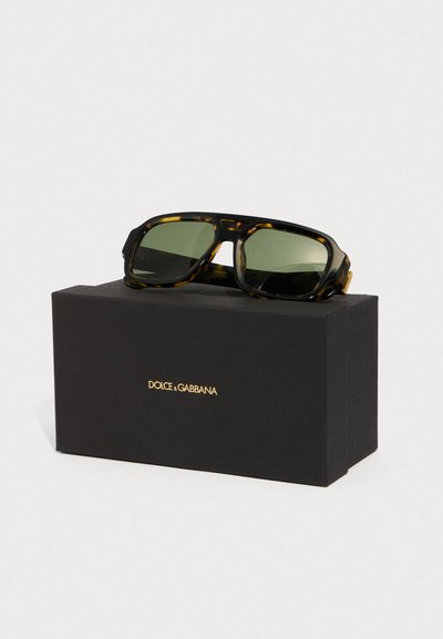 Kočičí brýle v želvovinovém designu se zelenými skly, s robustním provedením. Představeno v černé krabičce se zlatým logem "Dolce & Gabbana".