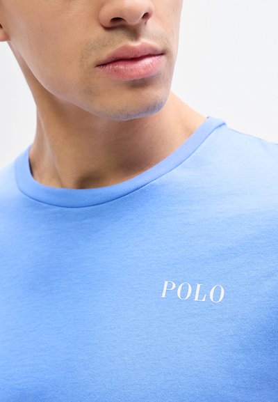 Κοντινό σε κάτω μέρος προσώπου και λαιμό ατόμου που φοράει γαλάζιο πουκάμισο με την επιγραφή "POLO" σε λευκό στο στήθος.