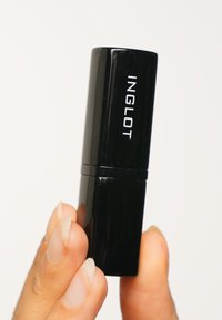 Étui à rouge à lèvres rectangulaire noir avec une texture lisse, affichant le logo blanc "INGLOT" sur le côté. Tenue entre les doigts.
