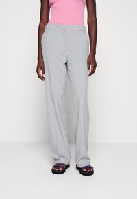 Szare spodnie w prążki o prostym kroju nogawek, z klasycznym stanem i wsuwanymi kieszeniami. Noszone z fioletowymi sandałami.