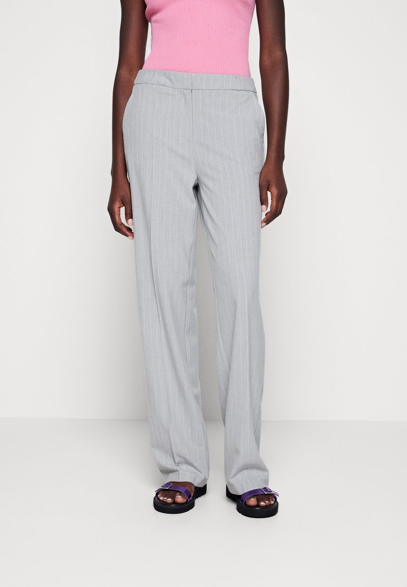 Szare spodnie w prążki o prostym kroju nogawek, z klasycznym stanem i wsuwanymi kieszeniami. Noszone z fioletowymi sandałami.