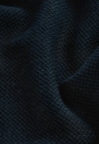 Dunkelblaues, strukturiertes Strickgewebe mit einem gewebten Muster, das eine weiche, leicht flauschige Oberfläche und ein komplexes Zusammenspiel von Schatten zeigt.
