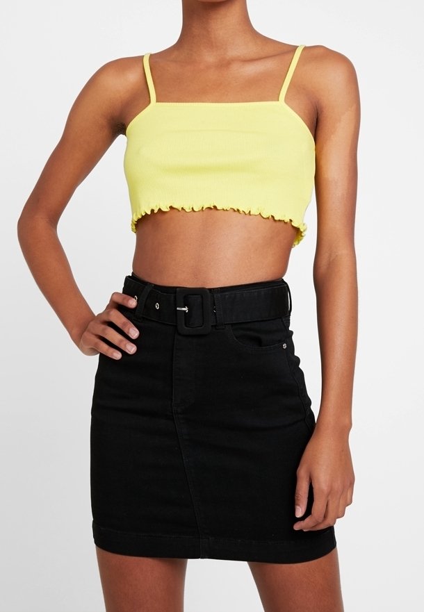 Top corto amarillo con tirantes finos y dobladillo volado, combinado con una falda de mezclilla negra de cintura alta que incluye un cinturón y bolsillos frontales.