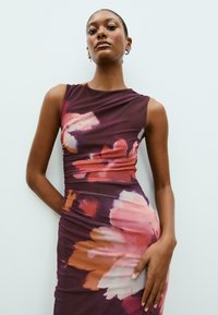 Kukkakuvioinen hihaton mekko, jossa on purppuran, vaaleanpunaisen ja oranssin sävyjä; rypytysjäykkyys; muotoon ommeltu design; sileä, joustava kangas.