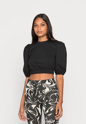 Blusa preta curta com mangas bufantes, tecido suave e bainha elástica; combinada com leggings de cintura alta em padrão mármore preto e branco.