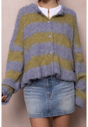 Gebreid vest met knopen en brede horizontale strepen in lavendel en olijfgroen, gedragen over een wit shirt en gecombineerd met een verveelde denim minirok.