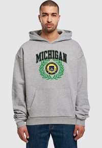 Szürke kapucnis felső, amelyen kék szöveggel szerepel a "MICHIGAN" felirat, valamint egy zöld és sárga kör alakú embléma középen az elején. Kanguru zsebet is tartalmaz.