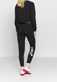 Zwarte sweatpants met taps toelopende benen, voorzien van een wit logo op de linkerdij. Gecombineerd met een zwart cropped sweatshirt, beide in een zachte stof.