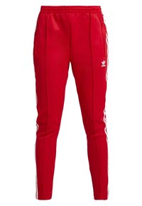 Röda sportiga joggingbyxor med sidofickor, elastisk midja och vita randiga detaljer. Tillverkade av ett mjukt tyg, med en logotyp på höften.