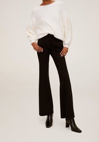 Pull en tricot blanc, ample et à épaules tombantes, associé à un pantalon noir évasé ajusté et des bottines noires à talons.