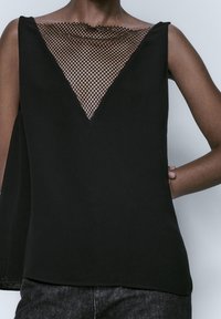 Haut noir avec un design en V en maille, tissu lisse et sans manches avec un ourlet droit. Pas d'embellissements ou de motifs supplémentaires.